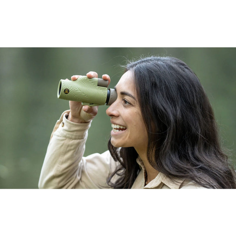 Load image into Gallery viewer, A woman outdoors holding a compact green binocular to her eye, wearing a beige jacket against a blurred green background.