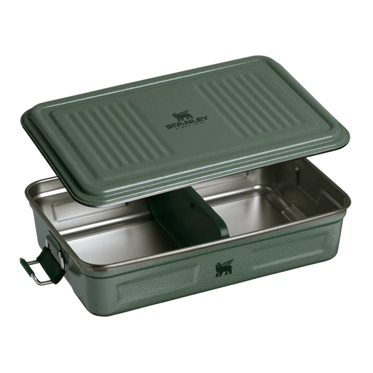A green Stanley food storage container with its lid propped open, showing a stainless steel interior and a dark green divider, on a white background.